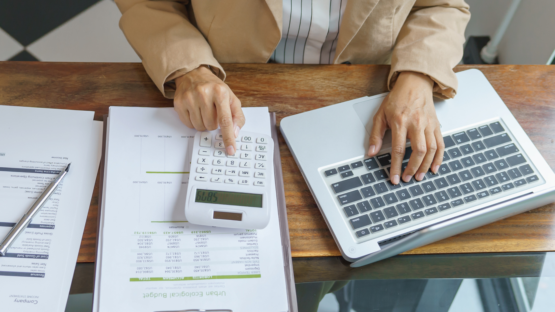 Remote Work Setup - Printed Excel sheet looking like an accounting sheet for business, with a person using a calculator. Remote Work Setup - Printed Excel sheet looking like an accounting sheet for business, with a person using a calculator.